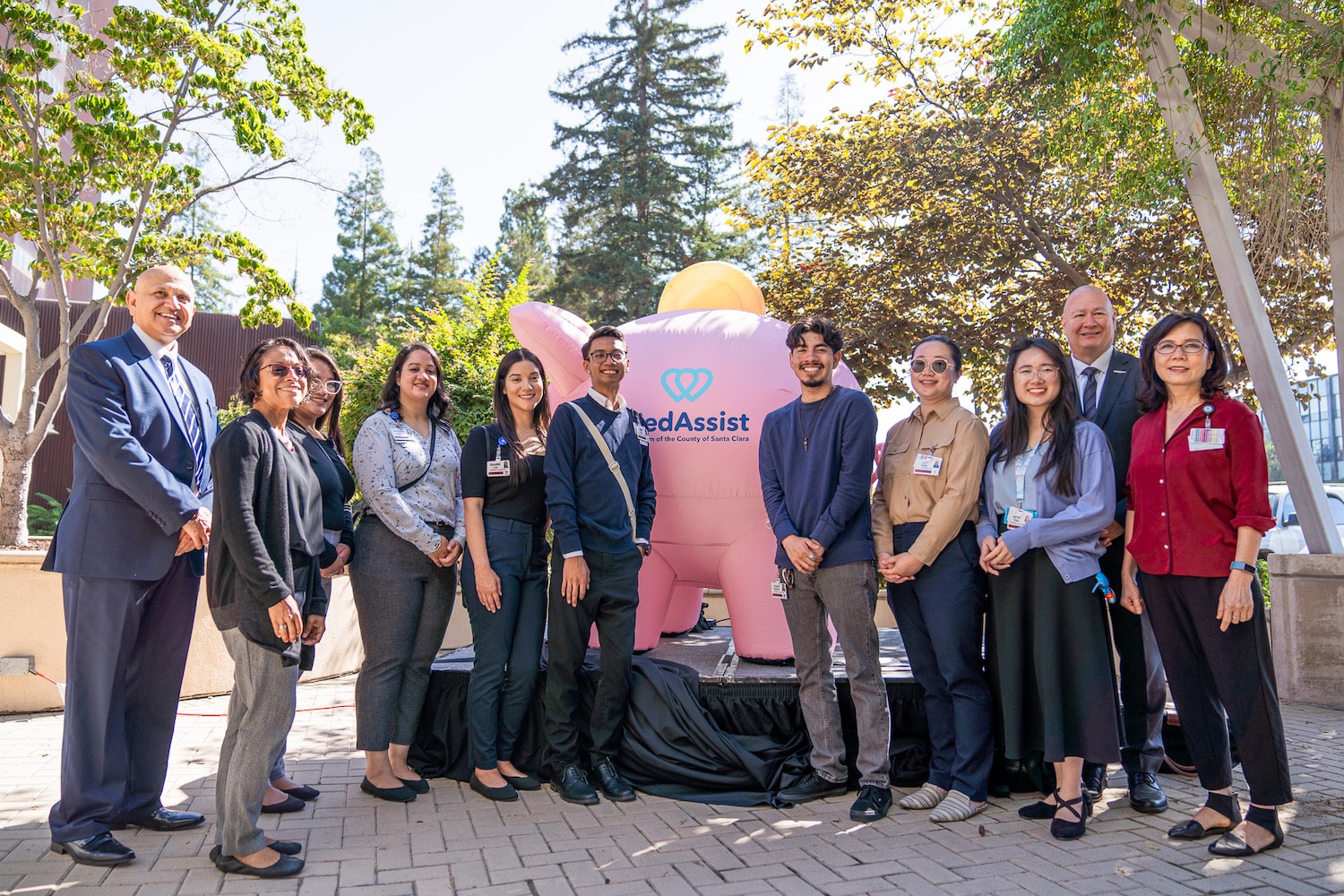 Group photo of MedAssist pharmacy team posing in front of inflatable Piggy Bank Mascot